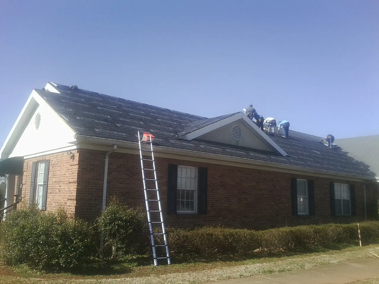 Crew tearing shingles off a brick ranch roof with a ladder set — Emergency Roof Repair work by our crew in Newton Hamilton