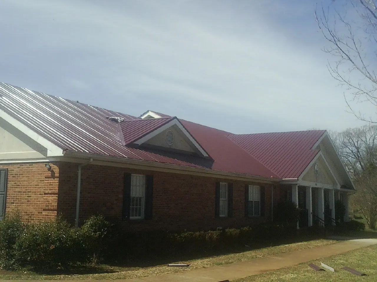 Red metal roof with gabled entries on a long brick building, from a Hail Damage Roof Repair job in Newton Hamilton