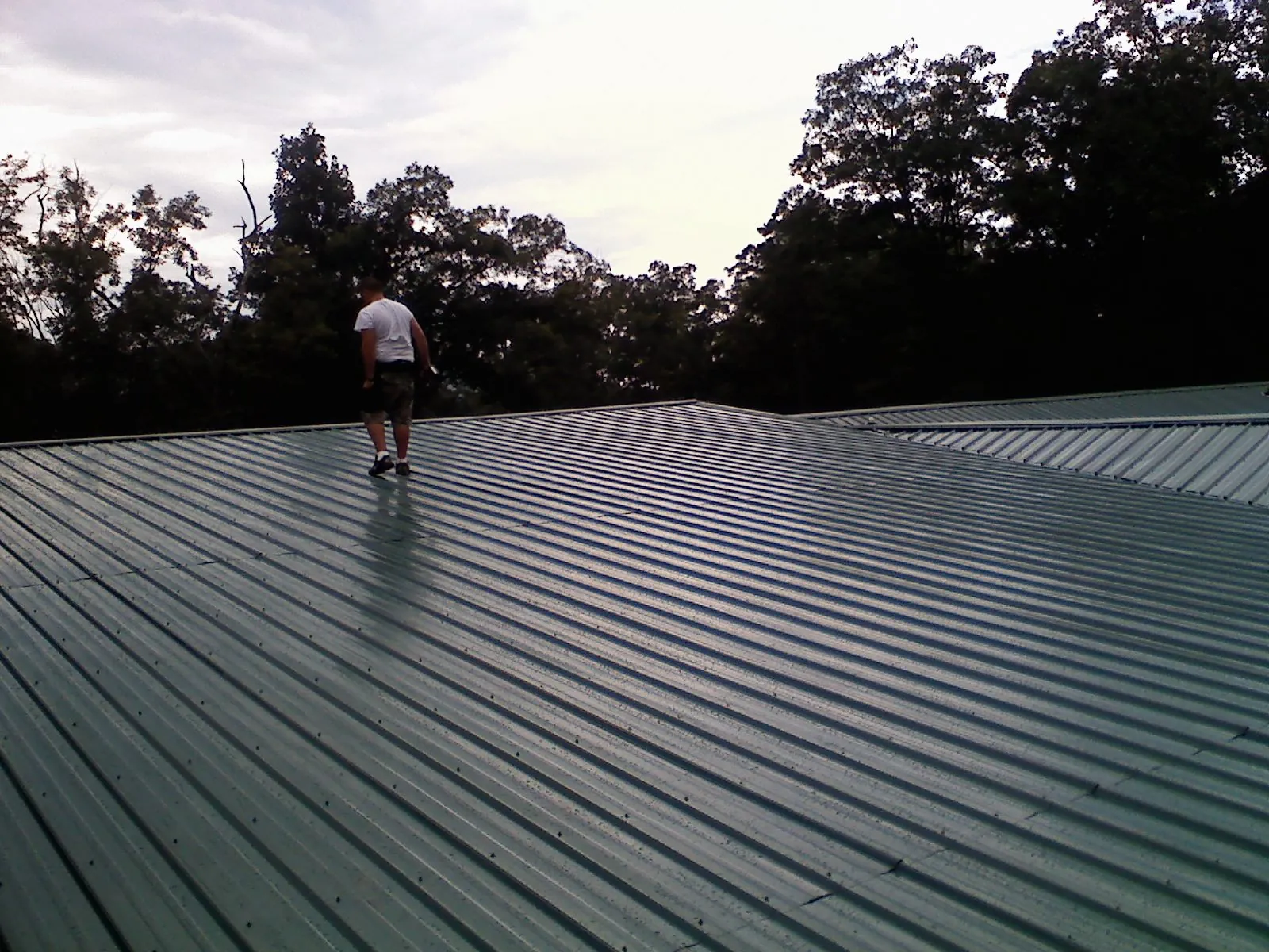 Roofer walking a wide expanse of new green metal roofing in Newton Hamilton