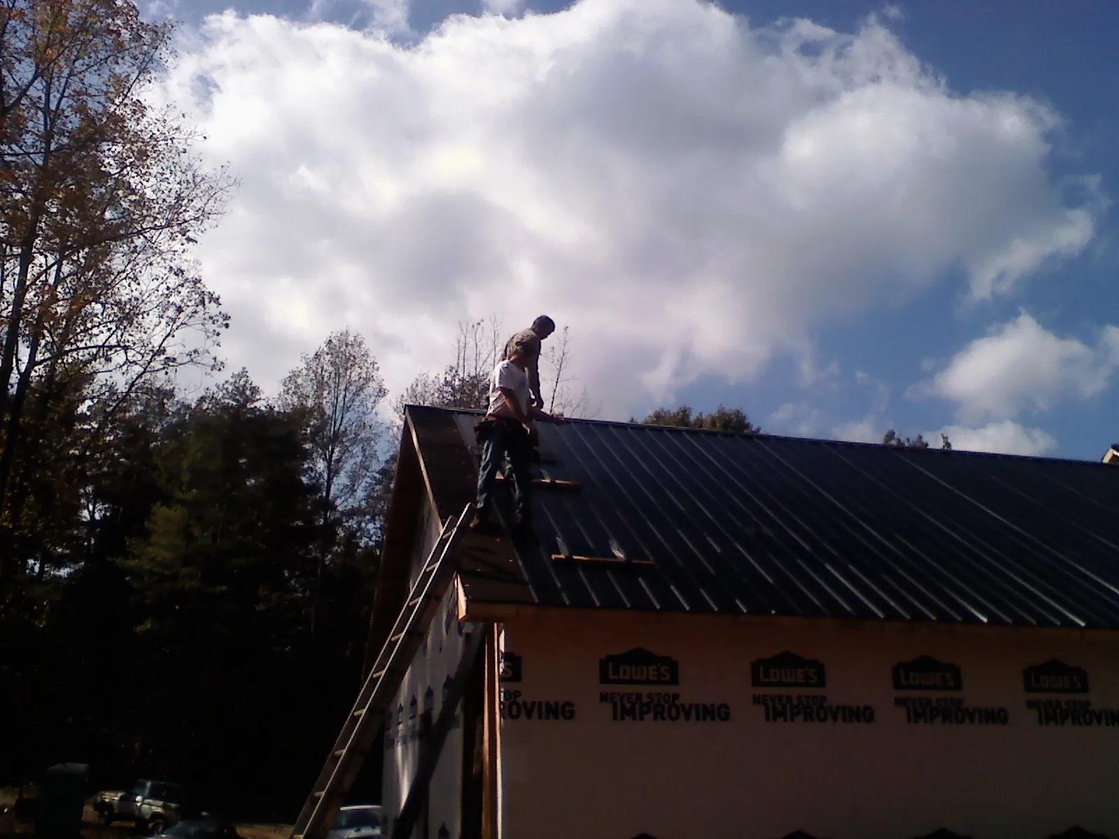 Roofer fastening dark metal panels high against a cloudy sky, from a Roof Inspection job in Newton Hamilton