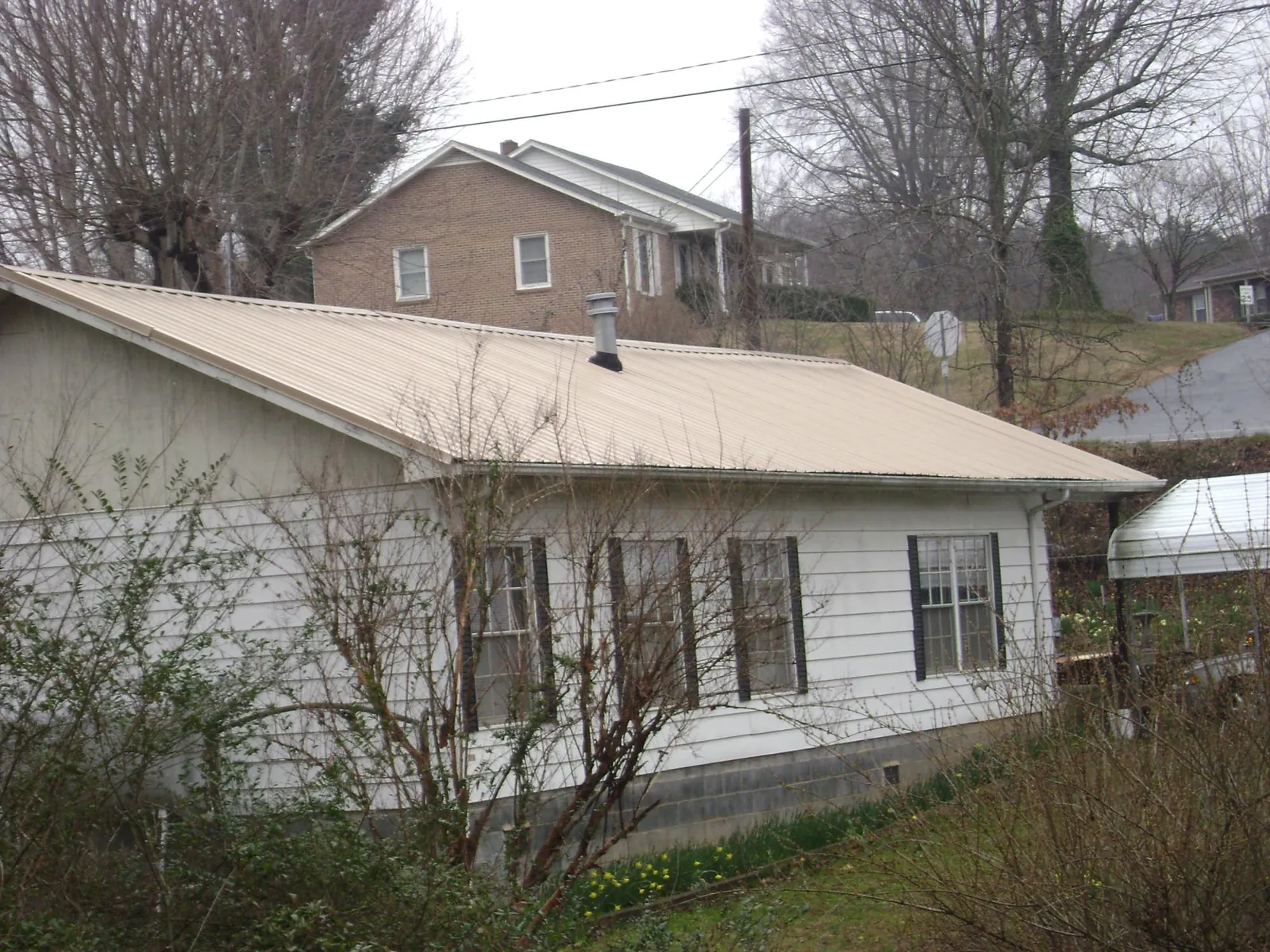 Tan metal roof on a white sided house set into a hillside — Commercial Roofing by Roofing Brothers in Newton Hamilton